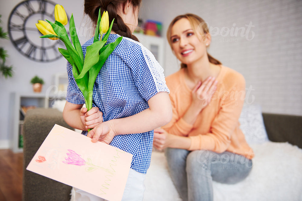 Girl holding flowers and greeting card behind her back