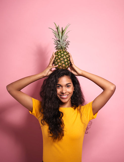 Beautiful African woman holding a pineapple on her head.