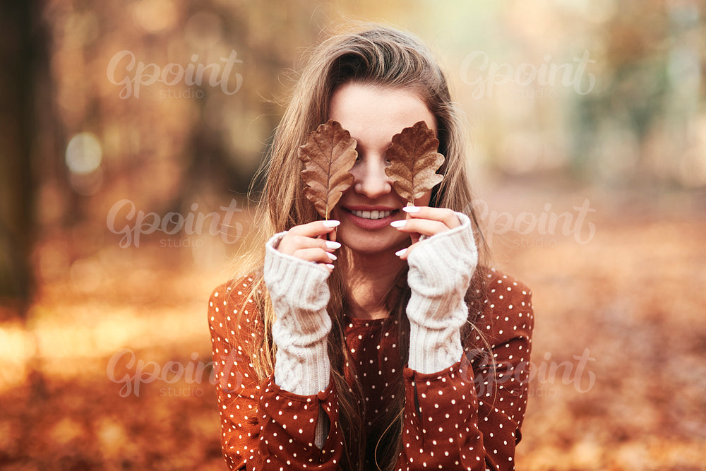 Woman covering eyes with autumnal leaves