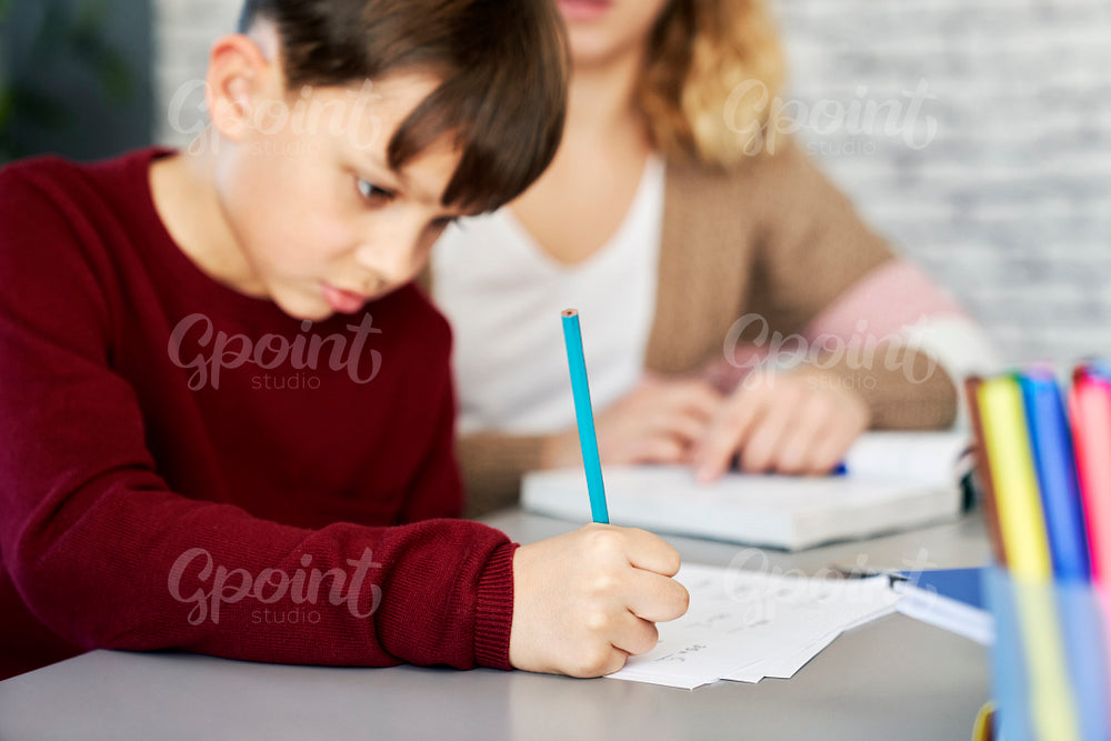 Close up of schoolboy doing homework at home with mom
