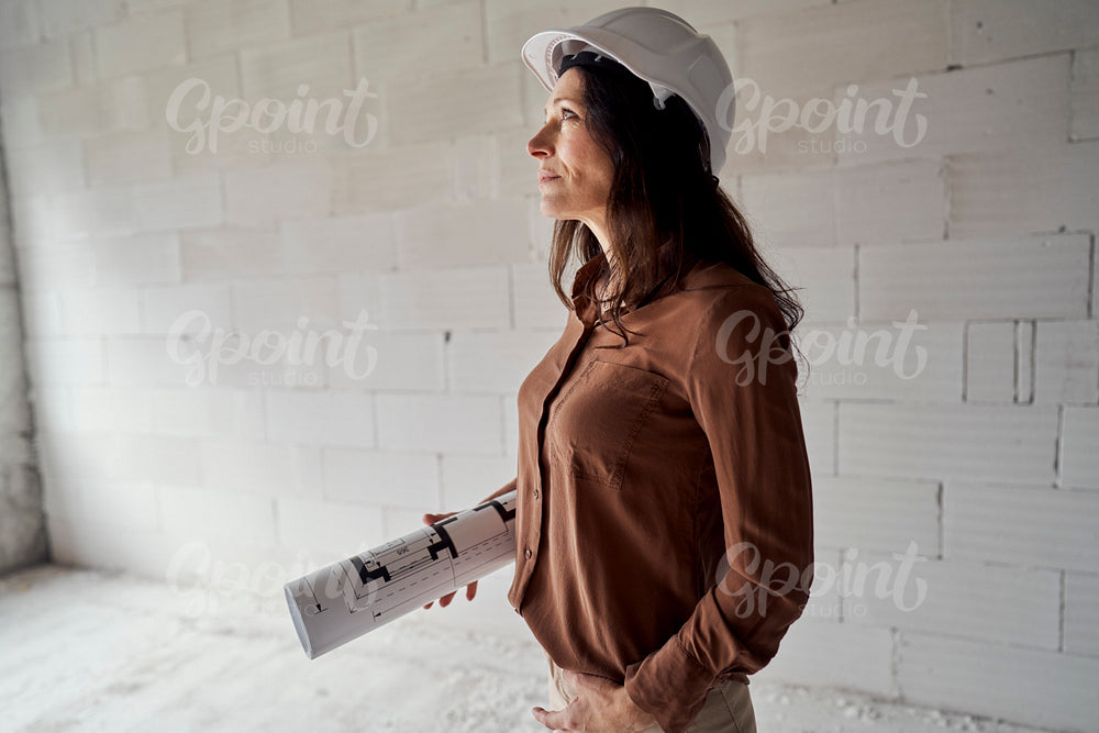 Female mature caucasian engineer standing on construction site and browsing building plans 