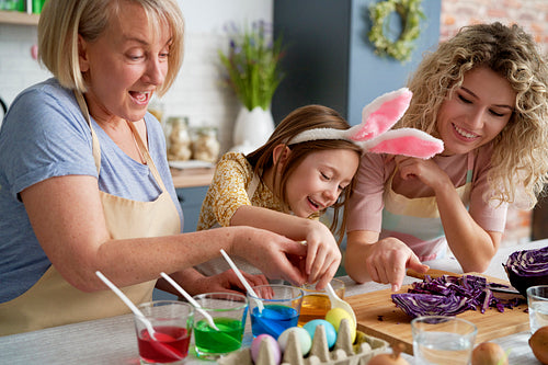 Little girl with mother and grandmother coloring Easter eggs