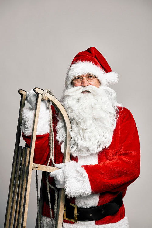 Portrait of caucasian Santa Claus with sled on grey background