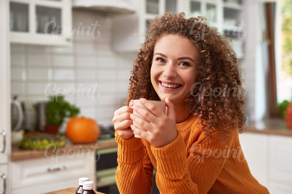Smiling young woman drinking hot tea in the kitchen