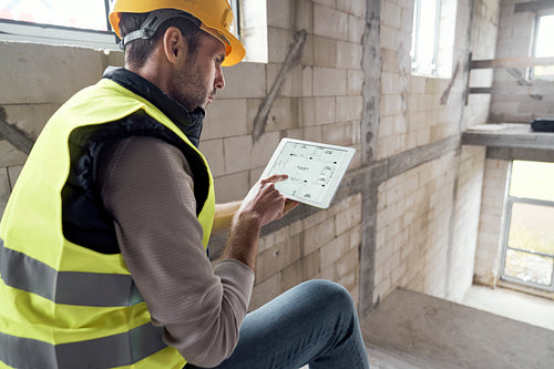 Caucasian engineer sitting on stairs and holding digital tablet on construction site