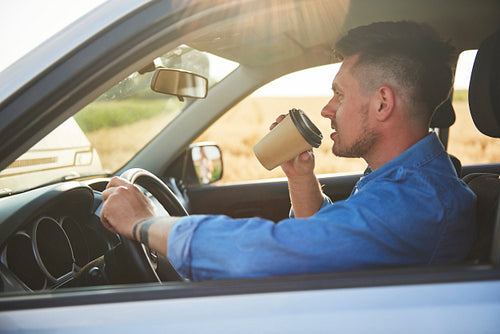 Young man driving a car and drinking coffee in a rush