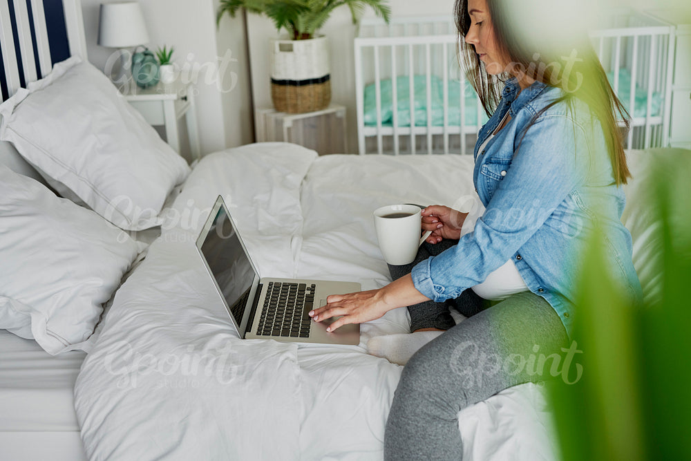 Pregnant woman sitting on bed and using a computer