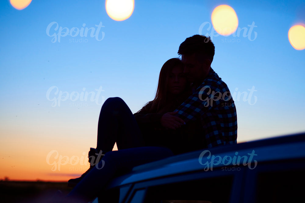 Loving couple embracing and sitting on car in the evening.