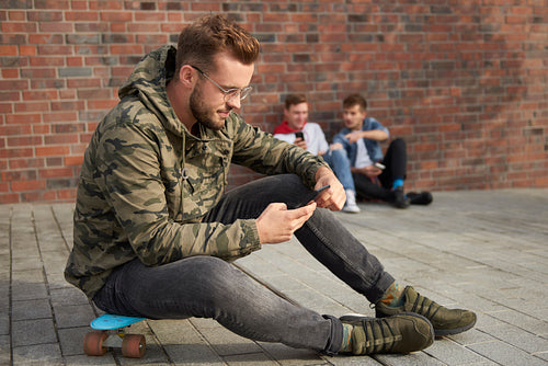 Handsome man using mobile phone and sitting on skateboard
