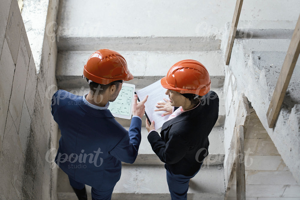 Female caucasian engineer and business woman holding document while walking stairs on construction site