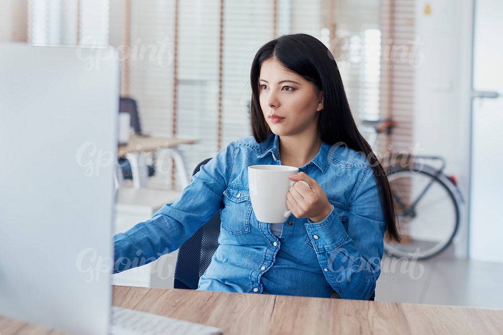 Asian woman drinking coffee and working on computer
