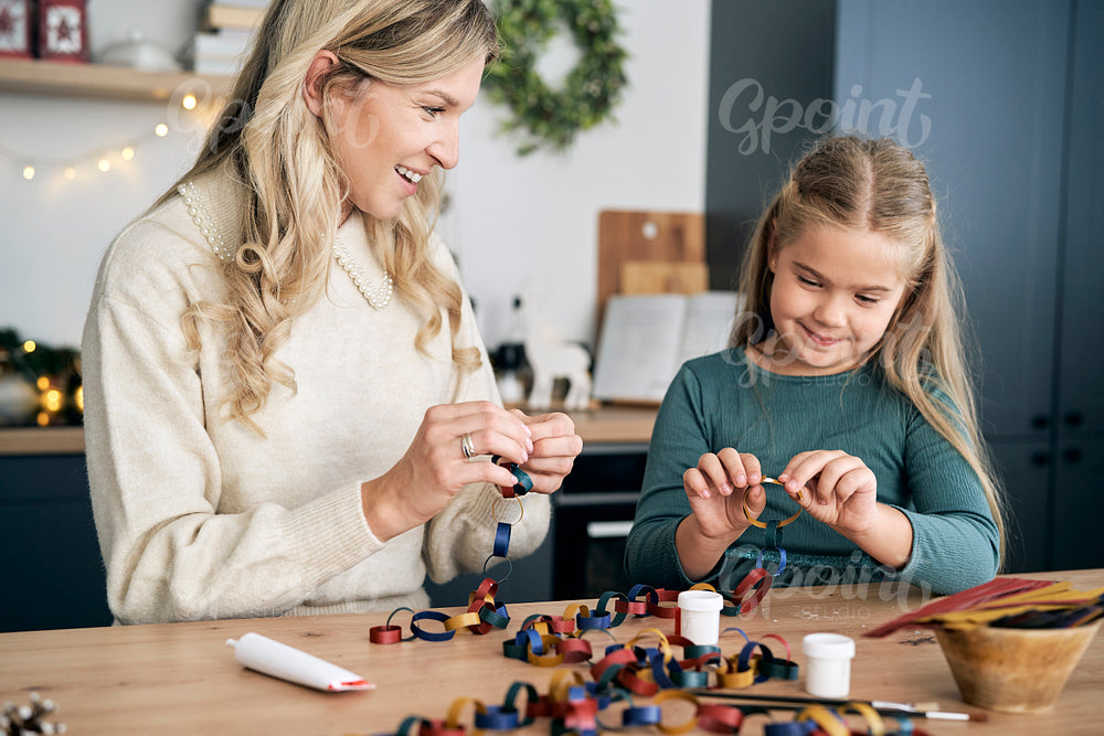 Caucasian girl and mother preparing DIY paper chain for Christmas tree and talking