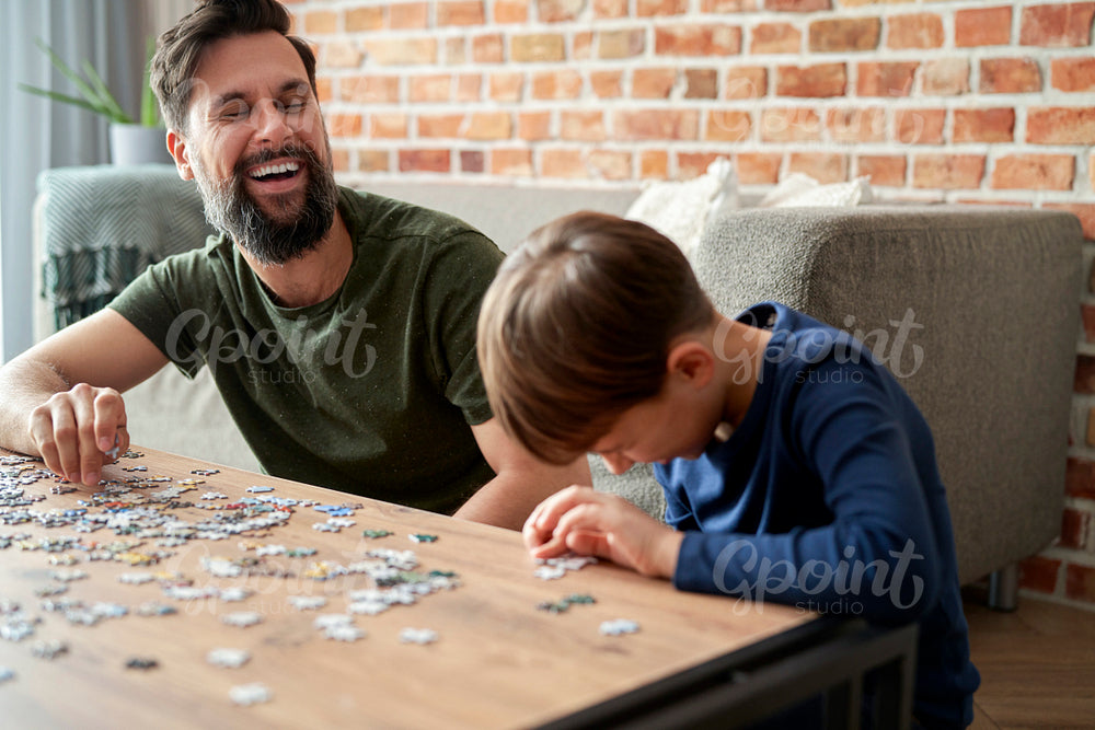 Happy son and father having fun during solving jigsaw puzzle