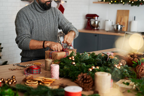 Man using decorative ribbon while making Christmas present