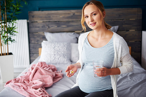 Portrait of young pregnant woman taking medicine and drinking water