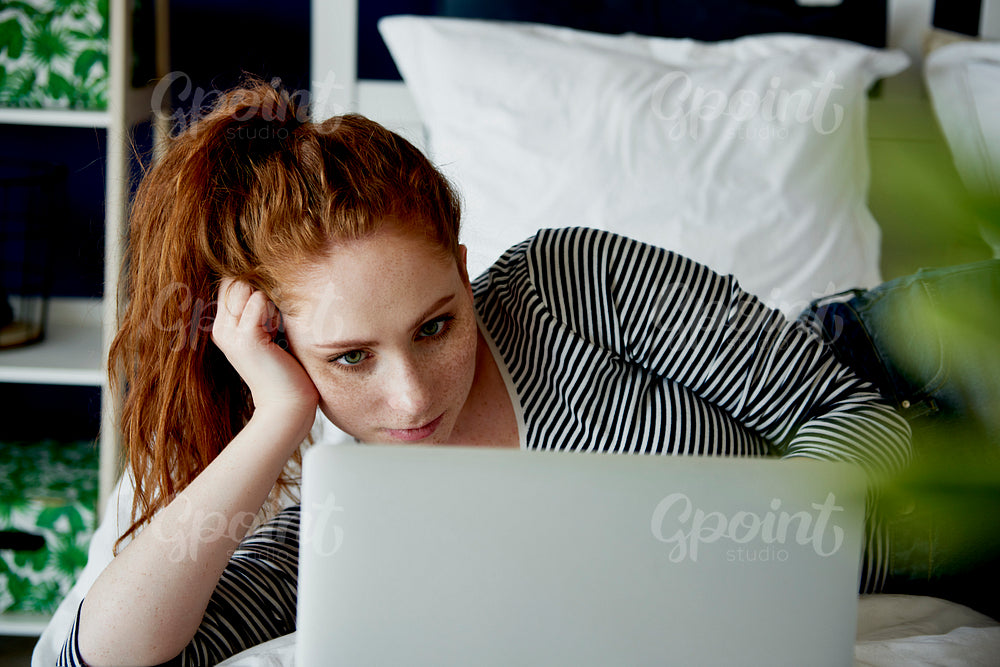 Bored woman using laptop in bed