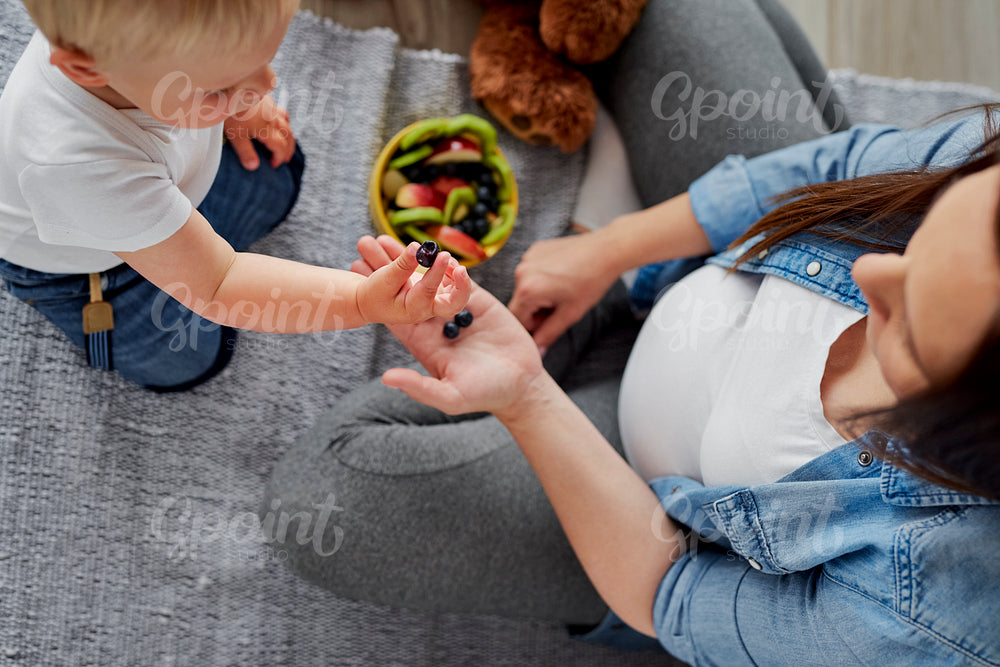 Mother convincing her baby son to eat some fruit