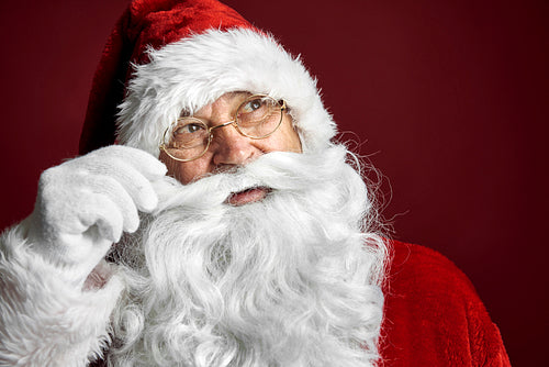 Smiling caucasian Santa Claus touching mustache on red background