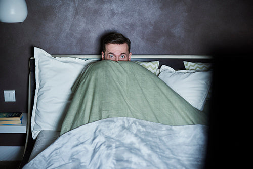 Scared man watching horror movies in bed