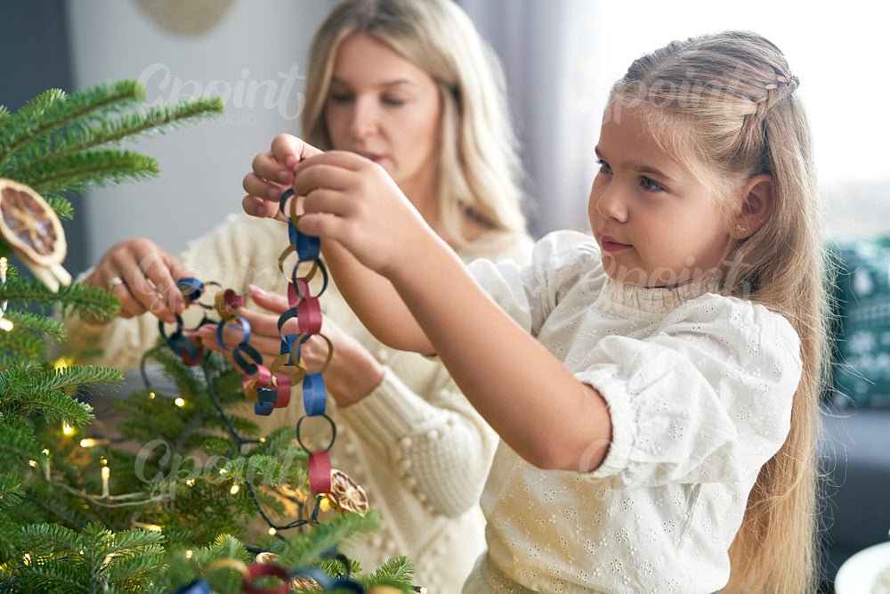 Caucasian little girl and mother decorating Christmas tree with DIY paper chain