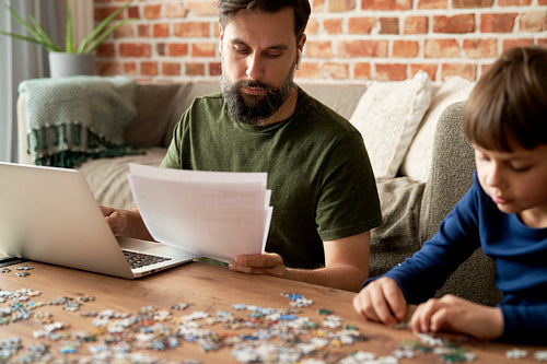 Son solving jigsaw puzzle during father working at home