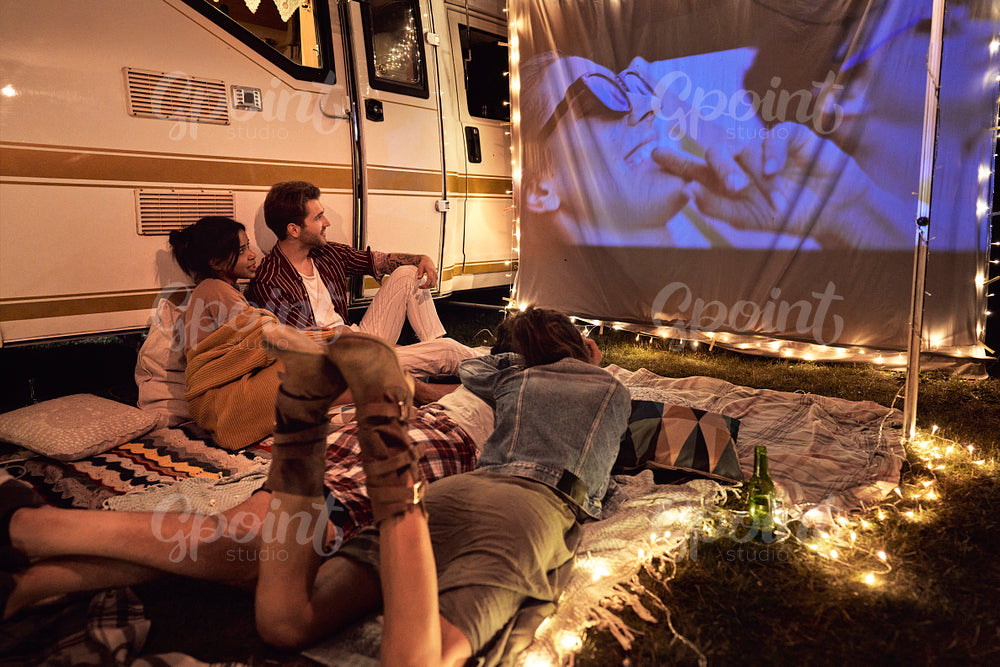 Happy group of young cheerful people watching a movie on camping site