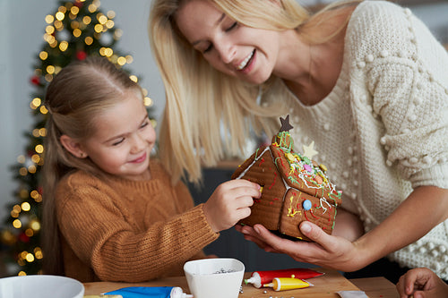 Mother helping children to decorate a gingerbread house
