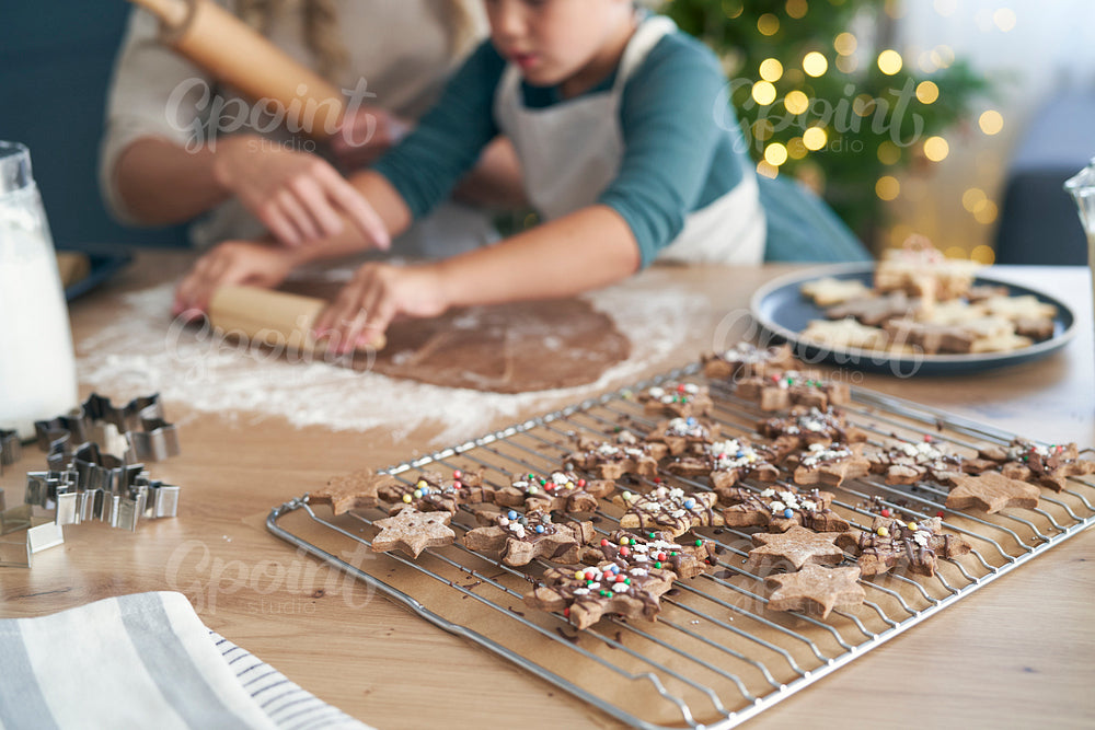 Decorated gingerbread cookies in the foreground and Caucasian woman with daughter making another of raw dough
