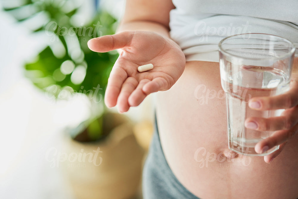 Pregnant woman holding a pill and glass of water