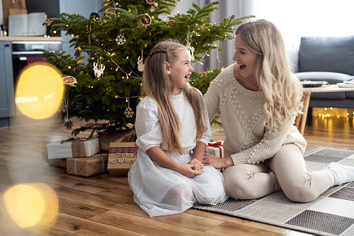 Caucasian girl and mother having fun while sitting next to Christmas tree
