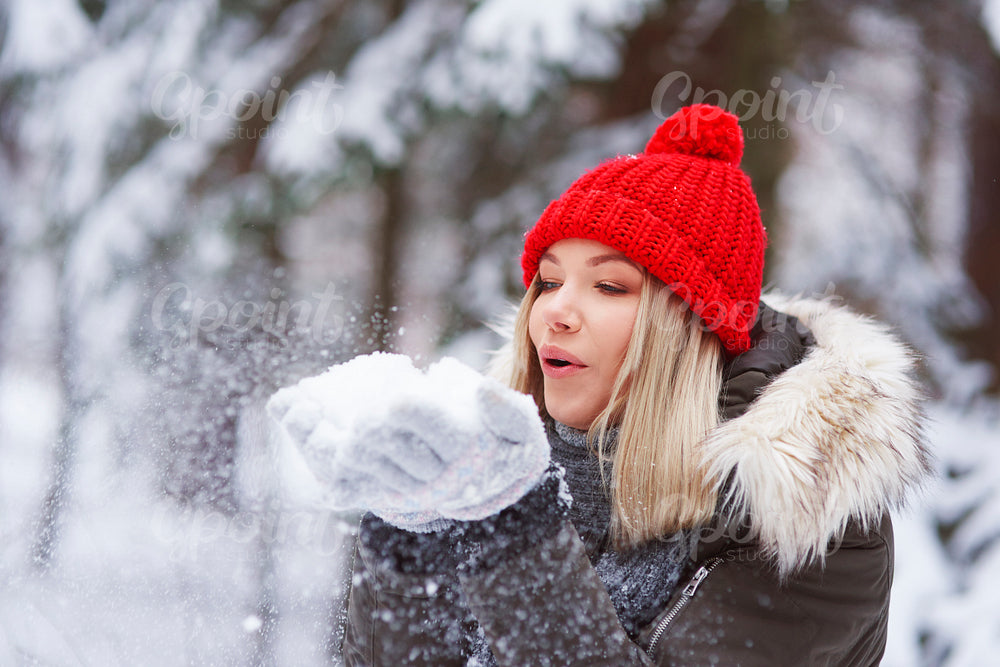 Beautiful young woman blowing snowflakes