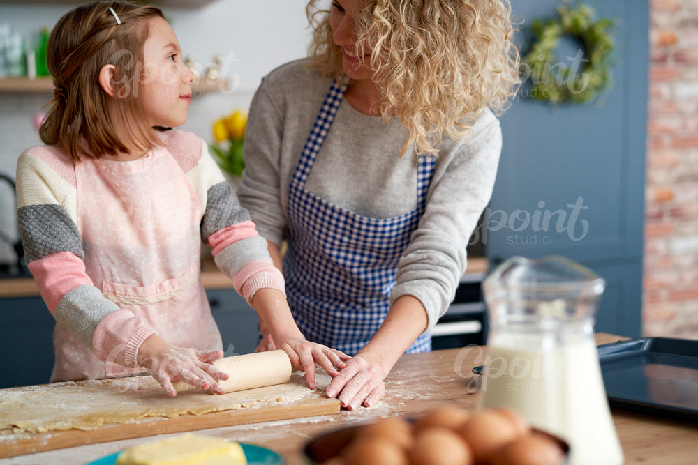 Little girl rolling dough with her mother int the kitchen