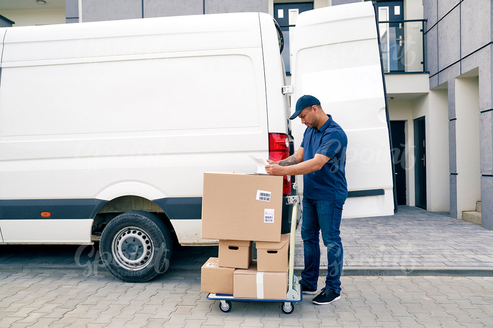 Courier with packages on a hand truck looking at documents