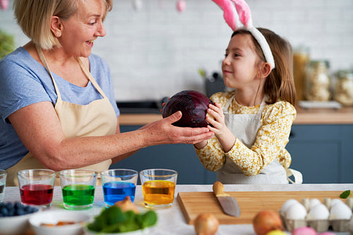 Little girl helping grandmother prepare natural dyes for coloring eggs