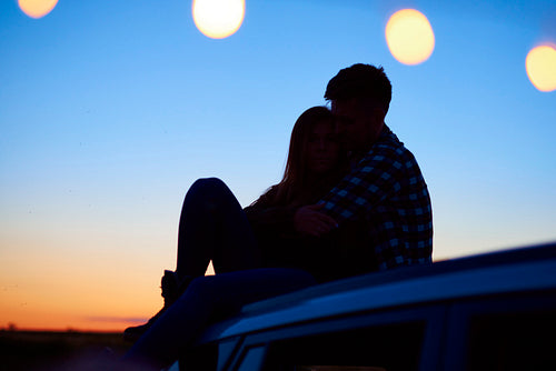 Loving couple embracing and sitting on car in the evening.