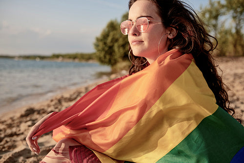 Young woman wrapped in rainbow flag on the beach