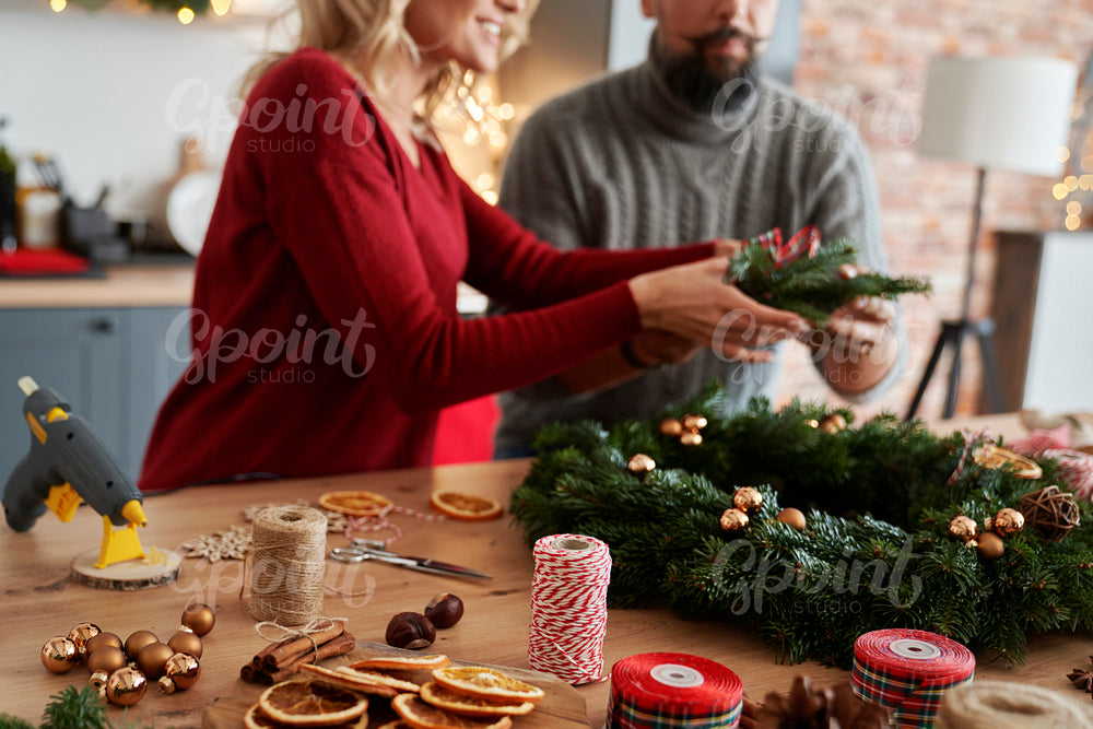 Couple making Christmas wreath at table full of decorations