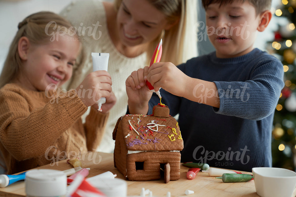 Children and mother decorating gingerbread house