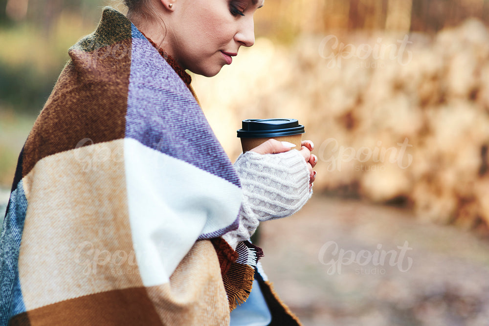 Woman warmly dressed holding coffee cup in the forest autumn
