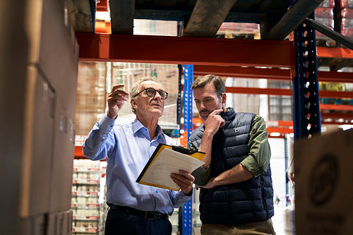 Two caucasian men in mature age discussing over documents together in warehouse