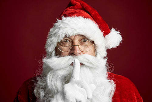 Santa Claus standing on the red background and showing quiet sign