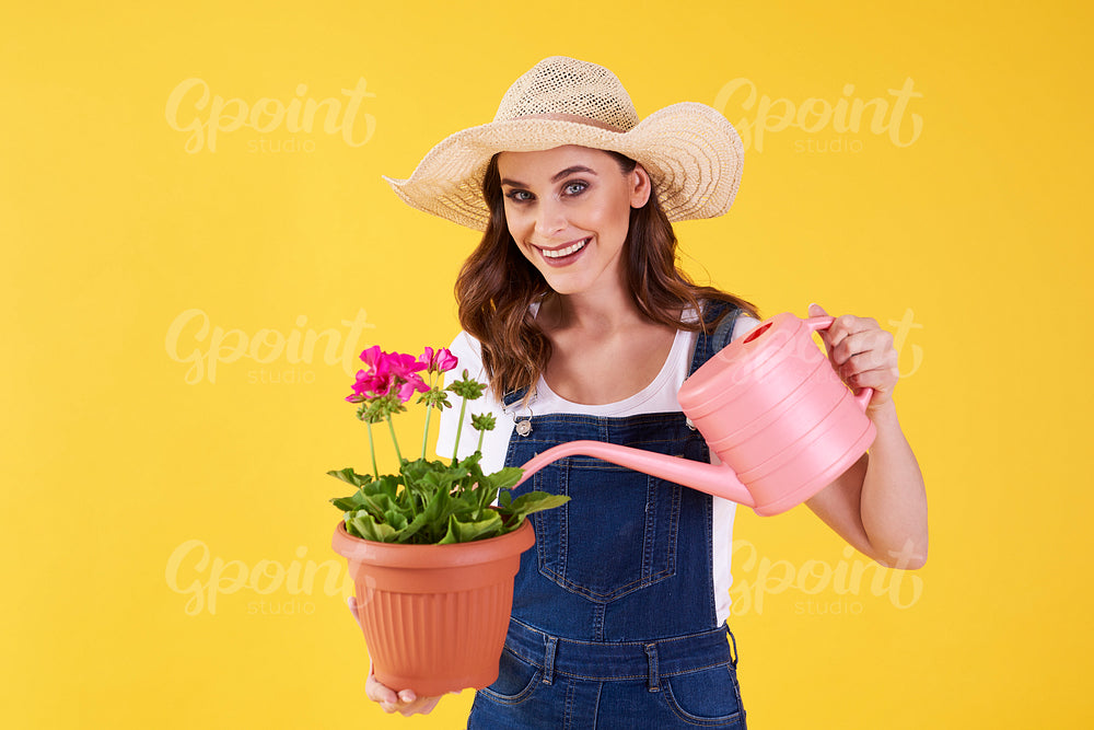 Smiling woman watering the flower in the studio shot