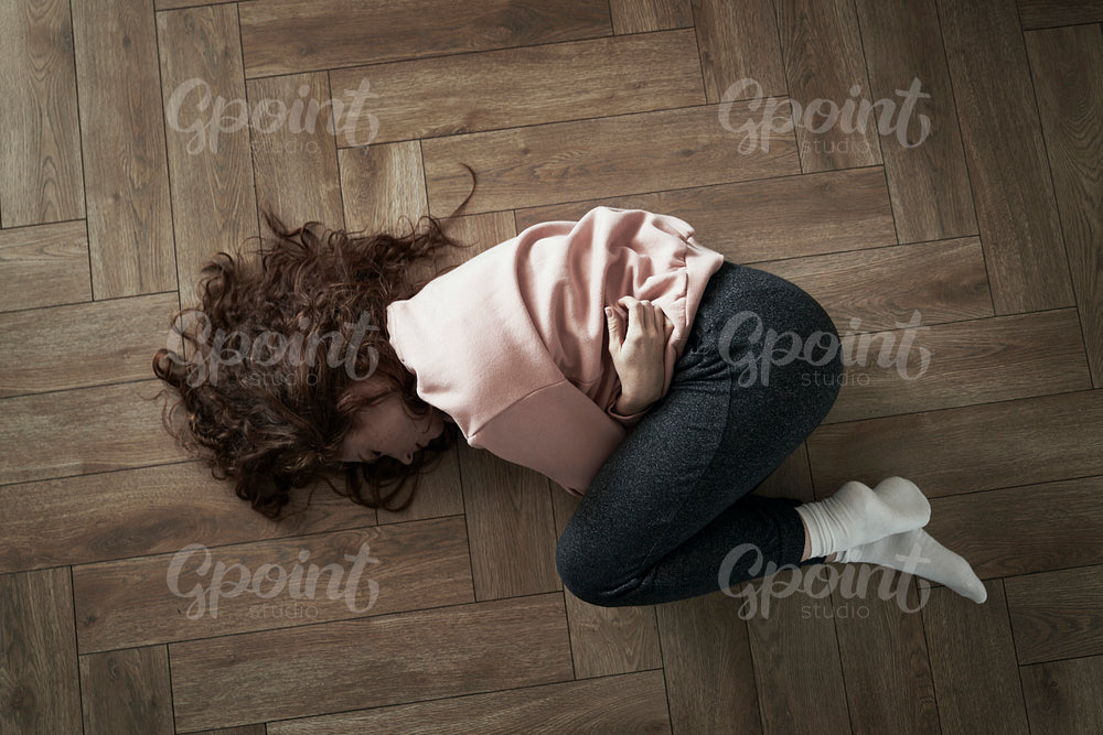 Top view of young caucasian woman lying on floor and having strong stomachache