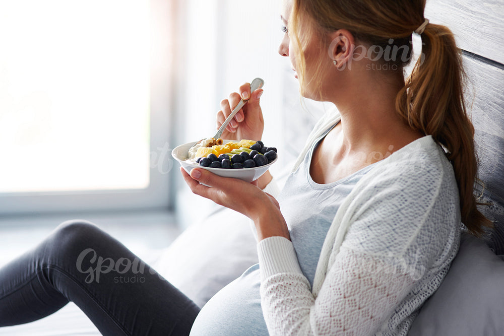 Side view of pregnant woman having breakfast at bedroom