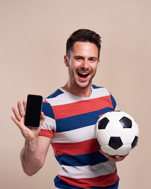 Excited fan holding soccer ball and showing mobile phone