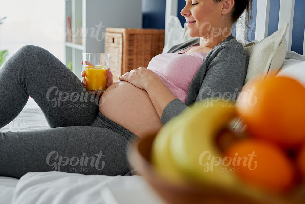 Pregnant woman drinking freshly pressed juice in bed