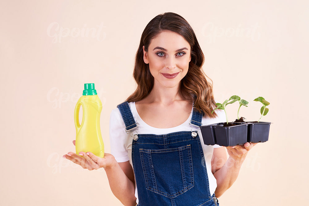 Portrait of beautiful woman holding cucumber seedling and fertilizer