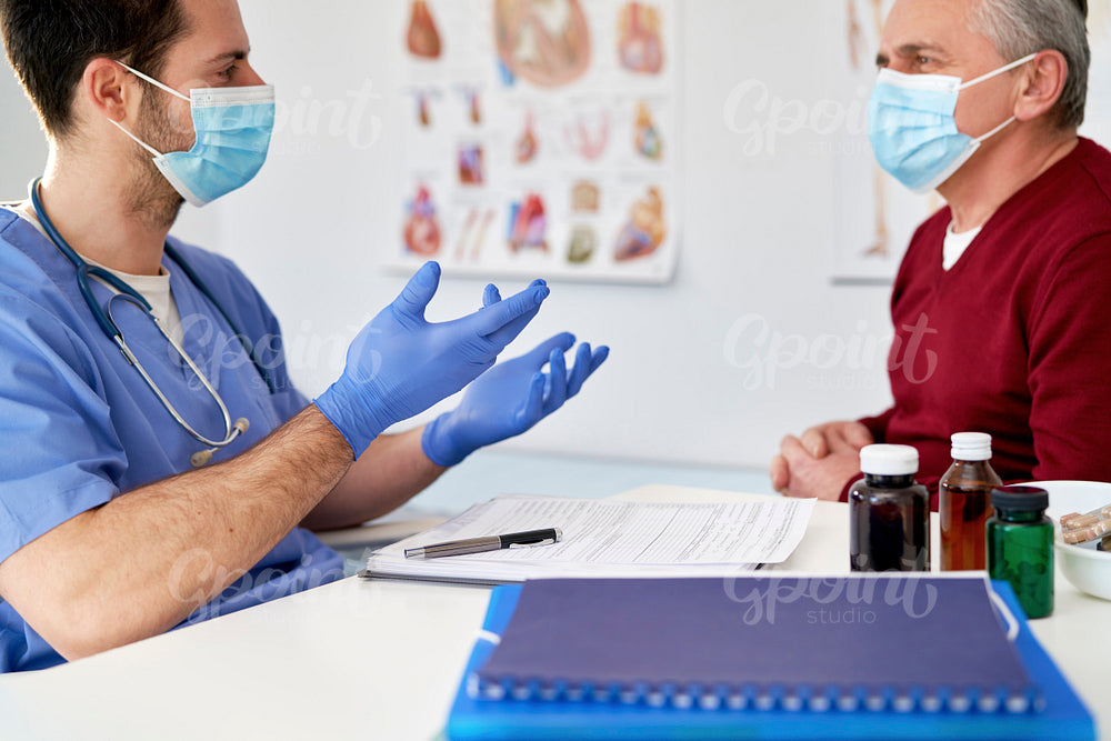 Doctor in protective mask talking with a senior patient