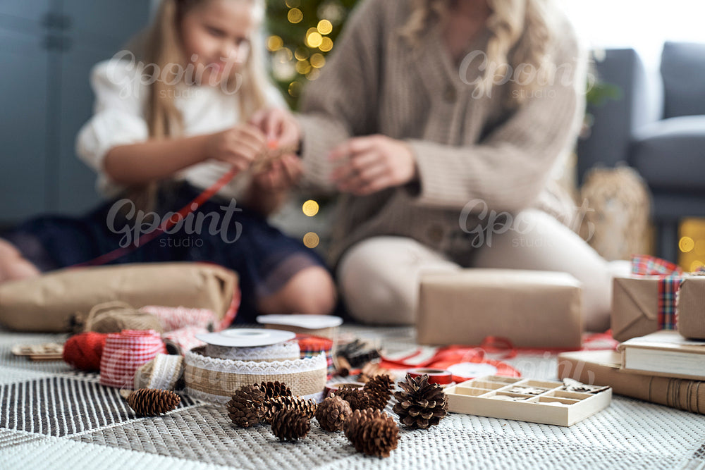 Christmas decorations on foreground and girl and mother wrapping Christmas gifts on floor in the background 