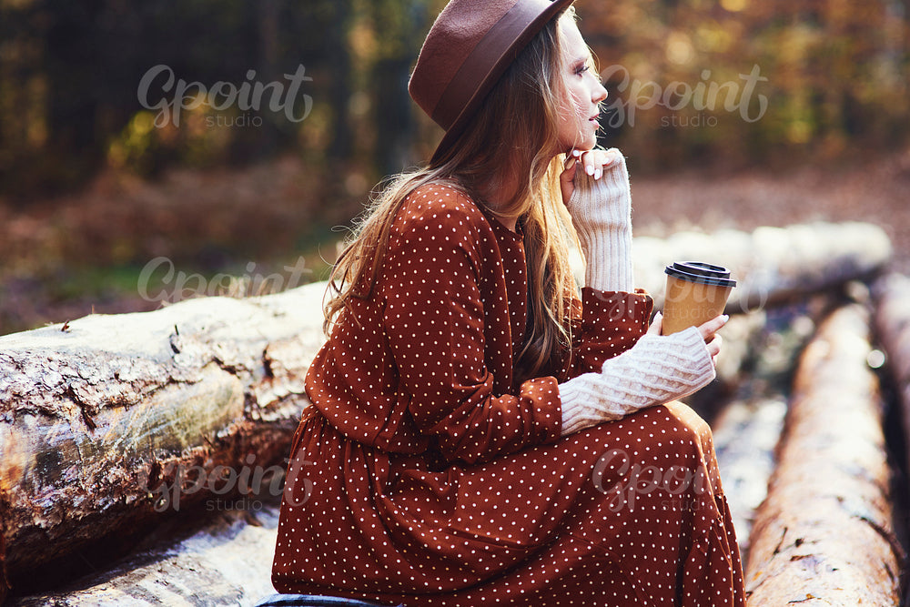 Side view of beautiful woman drinking coffee in autumn forest